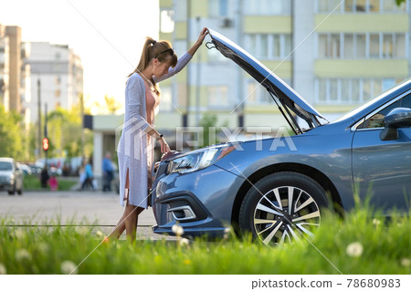 Helpless woman standing near her car with open bonnet inspecting broken motor. Young female driver having trouble with vehicle. Helpless woman standing near her car with open bonnet inspecting broken motor. Young female driver having trouble with vehicle. 78680983