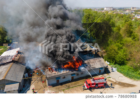 Aerial view of firefighters extinguishing ruined building on fire with collapsed roof and rising dark smoke. 78680988