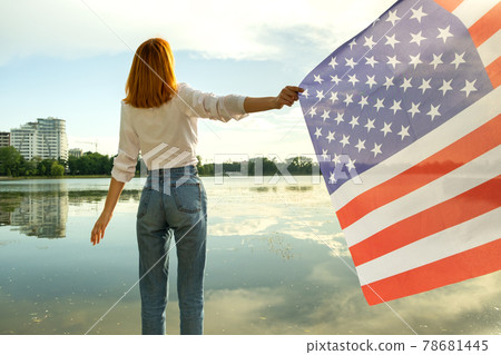 Young womanl with USA national flag on her shoulders with high city buildings in background celebrating United States independence day. International day of democracy concept. Young womanl with USA national flag on her shoulders with high city buildings in background celebrating United States independence day. International day of democracy concept. 78681445