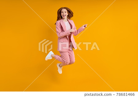 Successful business woman in suit jumping pinting index finger at side, isolated on yellow background 78681466