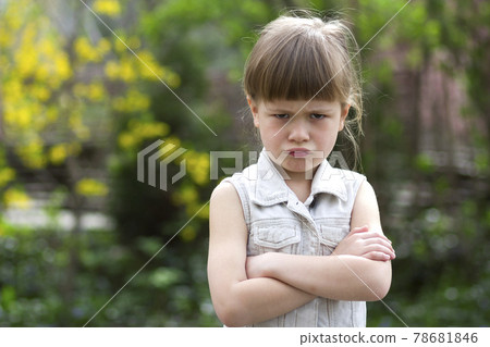 Pretty funny moody little blond preschool girl in white sleeveless dress looks into camera feeling angry and unsatisfied on blurred summer background. Children tantrum concept. 78681846