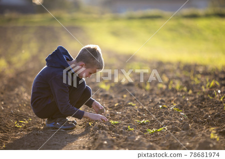 Young blond serious tired child boy squatting alone in empty field after harvest on late summer or autumn day on blurred sunny background. Hard peasant labor concept. 78681974
