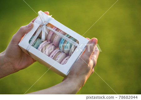 Female hands holding cardboard gift box with colorful pink blue handmade macaron cookies on green blurred copy space background. 78682044