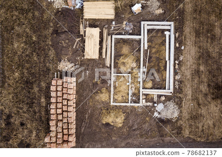 Concrete foundation for basement of future house, stacks of bricks and building timber logs for construction on sunny summer day, aerial view. Concrete foundation for basement of future house, stacks of bricks and building timber logs for construction on sunny summer day, aerial view. 78682137