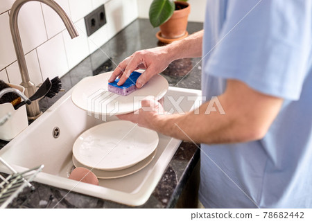 Unrecognizable male hands washing dishes at kitchen sink while doing cleaning at home at weekends 78682442