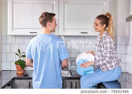 Happy caucasian woman wiping dishes while husband washing at kitchen Happy caucasian woman wiping dishes while husband washing at kitchen 78682466