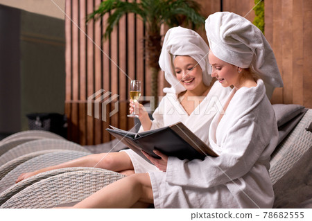 Girlfriends in bath towels communicating in spa salon while drinking champagne 78682555