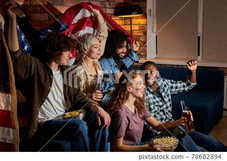 Excited multicultural american friends soccer fans gathered together at home in dark room watching on tv sportive game 78682894