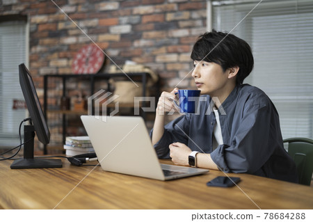 A man in his twenties looking at a computer screen with a mug A man in his twenties looking at a computer screen with a mug 78684288