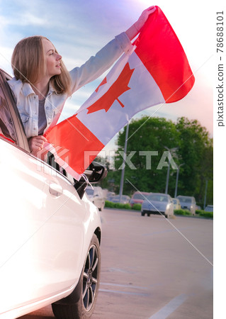 Young millennial blonde woman holding The National Flag of Canada looking from car window. Canadian Flag or the Maple Leaf. Tourist traveler or patriotism. Immigrant in a free country. Independence 78688101