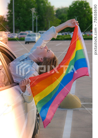 Young blonde millennial woman with LGBTQ flag looking from car window. Rainbow LGBT flag. Peace and freedom the symbol of LGBT, spending and sharing loving time. Support LGBTQ community 78688690