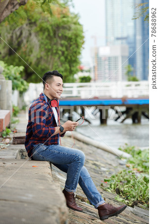 Dreamy Asian Man Choosing Track on Smartphone 78688962