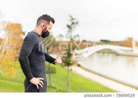 Young runner man with mask and headphones checking stopwatch. 78689529