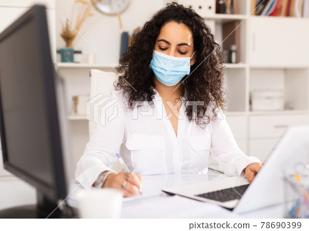 Woman in protective mask worker is working with documents and laptop in office Woman in protective mask worker is working with documents and laptop in office 78690399