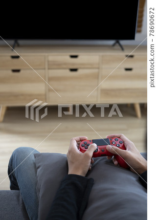 Man sitting on sofa and hold joystick and playing video games. 78690672