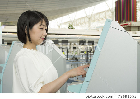 A woman operating a self-check-in machine at the airport 78691552