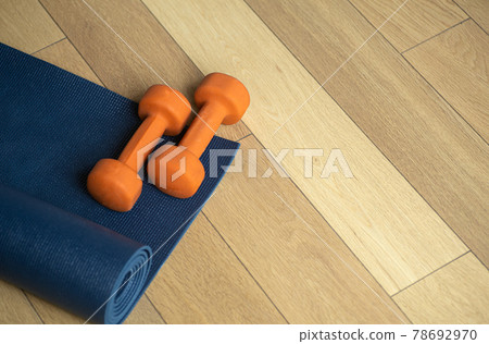 Yoga and fitness background. Wooden floor parquet or laminate with rug and dumbbells for training in a yoga room or gym Yoga and fitness background. Wooden floor parquet or laminate with rug and dumbbells for training in a yoga room or gym 78692970