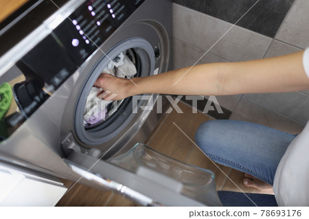Female hands getting out clean clothes from washing machine in bathroom Female hands getting out clean clothes from washing machine in bathroom 78693176