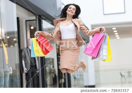 Emotionally happy woman jumping with shopping bags in mall Emotionally happy woman jumping with shopping bags in mall 78693357