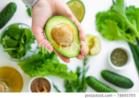 Woman cooking salad of fresh green vegetables and herbs. Raw food concept. Vegan menu. Cooking healthy diet or vegetarian food. Female hands hold avocado surrounded by green vegetables. Step by step 78693705
