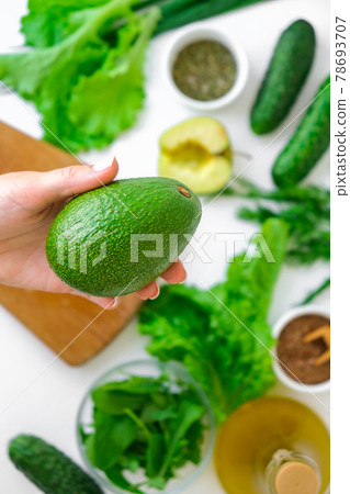 Woman cooking salad of fresh green vegetables and herbs. Raw food concept. Vegan menu. Cooking healthy diet or vegetarian food. Female hands hold avocado surrounded by green vegetables. Step by step Woman cooking salad of fresh green vegetables and herbs. Raw food concept. Vegan menu. Cooking healthy diet or vegetarian food. Female hands hold avocado surrounded by green vegetables. Step by step 78693707