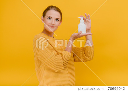 Beautiful pretty woman casually dressed uses an antiseptic sanitizer or liquid soap, calmly looks at the camera, Hygiene, cleaning concept standing isolated against a yellow background 78694042
