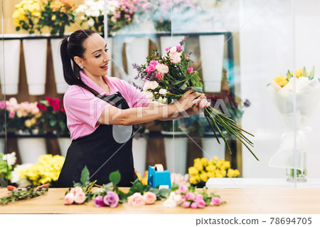 An attractive young female florist works in a flower shop and makes flower arrangements for sale 78694705