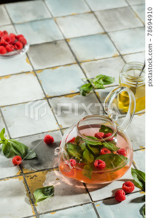 Hot raspberry tea in transparent teapot on a stone table. Fresh berries, mint, glass cup Hot raspberry tea in transparent teapot on a stone table. Fresh berries, mint, glass cup 78694910