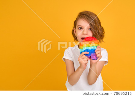 little girl holding pop it antistress toy on yellow background 78695215