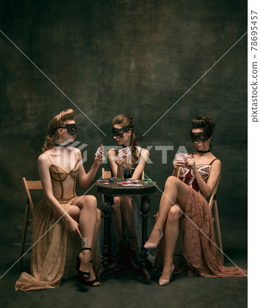 Pretty women in vintage 20s dresses. Young girls in art action sitting together and posing on wall background. 78695457