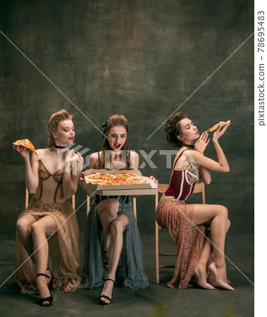 Pretty women in vintage 20s dresses. Young girls in art action sitting together and posing on wall background. 78695483