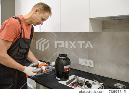 The worker is installing a household waste shredder for the kitchen sink. 78695845