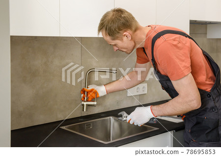 The plumber is installing a faucet on the kitchen sink. The plumber is installing a faucet on the kitchen sink. 78695853