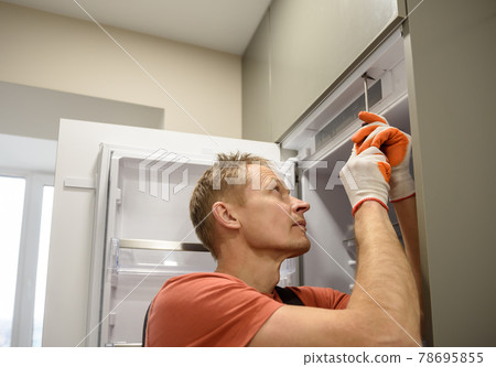 The worker is fixing the built-in refrigerator in the kitchen furniture. The worker is fixing the built-in refrigerator in the kitchen furniture. 78695855