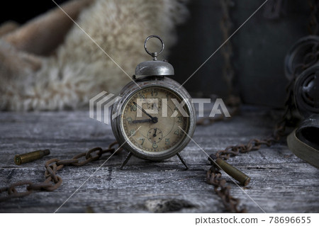 Vintage clock resting on wooden surface with military gas mask and rusty chains in background 78696655