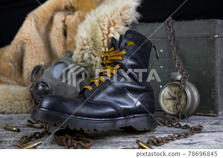 Leather boot with rusted chains and bullet shells with military gas mask and fur coat in background resting on wooden table 78696845