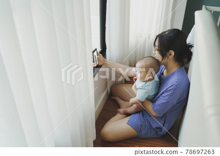 Asian mother and newborn baby boy doing online video call with family on smartphone  78697263