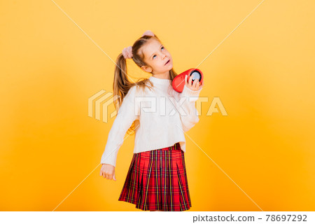 Young girl with portable wireless speaker enjoying and dancing on yellow background. 78697292