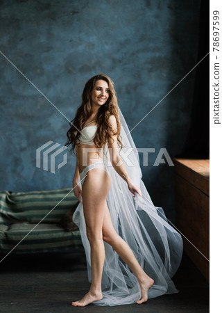 Beautiful woman in lingerie showing long legs sexy pose standing at bed over her bedroom near big window. Bride boudoir. Wedding morning. 78697599