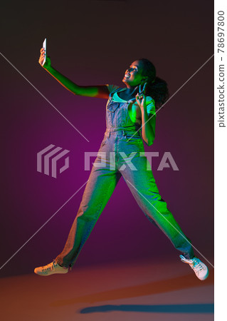 Latino young woman with phone isolated on studio background in neon. Concept of human emotions, facial expression. 78697800