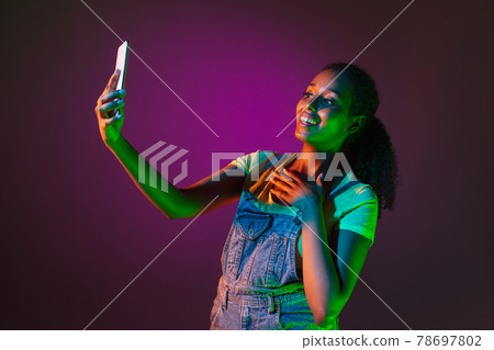 Latino young woman with phone isolated on studio background in neon. Concept of human emotions, facial expression. Latino young woman with phone isolated on studio background in neon. Concept of human emotions, facial expression. 78697802