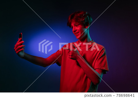 Caucasian young man with phone isolated on blue studio background in neon. Concept of human emotions, facial expression. 78698641
