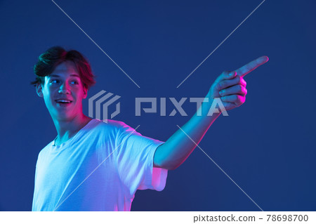 Caucasian young man's portrait on dark studio background in neon. Concept of human emotions, facial expression. Caucasian young man's portrait on dark studio background in neon. Concept of human emotions, facial expression. 78698700