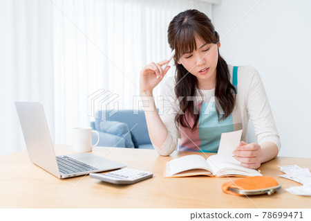A woman who keeps a household account book while checking the receipt and is worried about making ends meet A woman who keeps a household account book while checking the receipt and is worried about making ends meet 78699471
