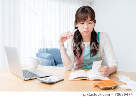 一位女士一邊查看收據一邊保留家庭賬簿,擔心入不敷出 一位女士一邊查看收據一邊保留家庭賬簿,擔心入不敷出 78699474