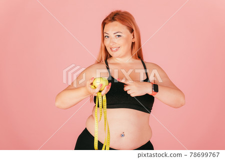 Portrait of beautiful oversized woman wearing sports outfit holding apple 78699767