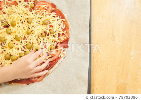 Childs hand with Pizza on baking paper prepared for baking. Cooking at home. 78702080