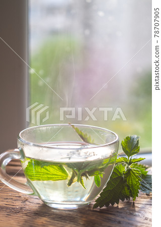 A cup of hot nettle tea and fresh nettles on a wooden board. 78707905
