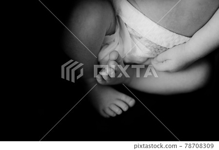 一張在黑暗的房間裡拍攝的可愛可愛的小新生嬰兒的手和腳的黑白照片。 78708309