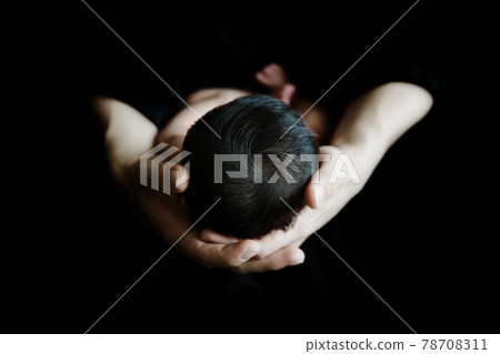 一個可愛可愛的小新生嬰兒的頭和父母的手在黑暗的空間裡拍攝 78708311